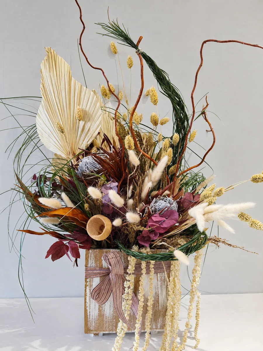 A dried arrangement with a bleached palm spear, bunny tails, protea and curly willow