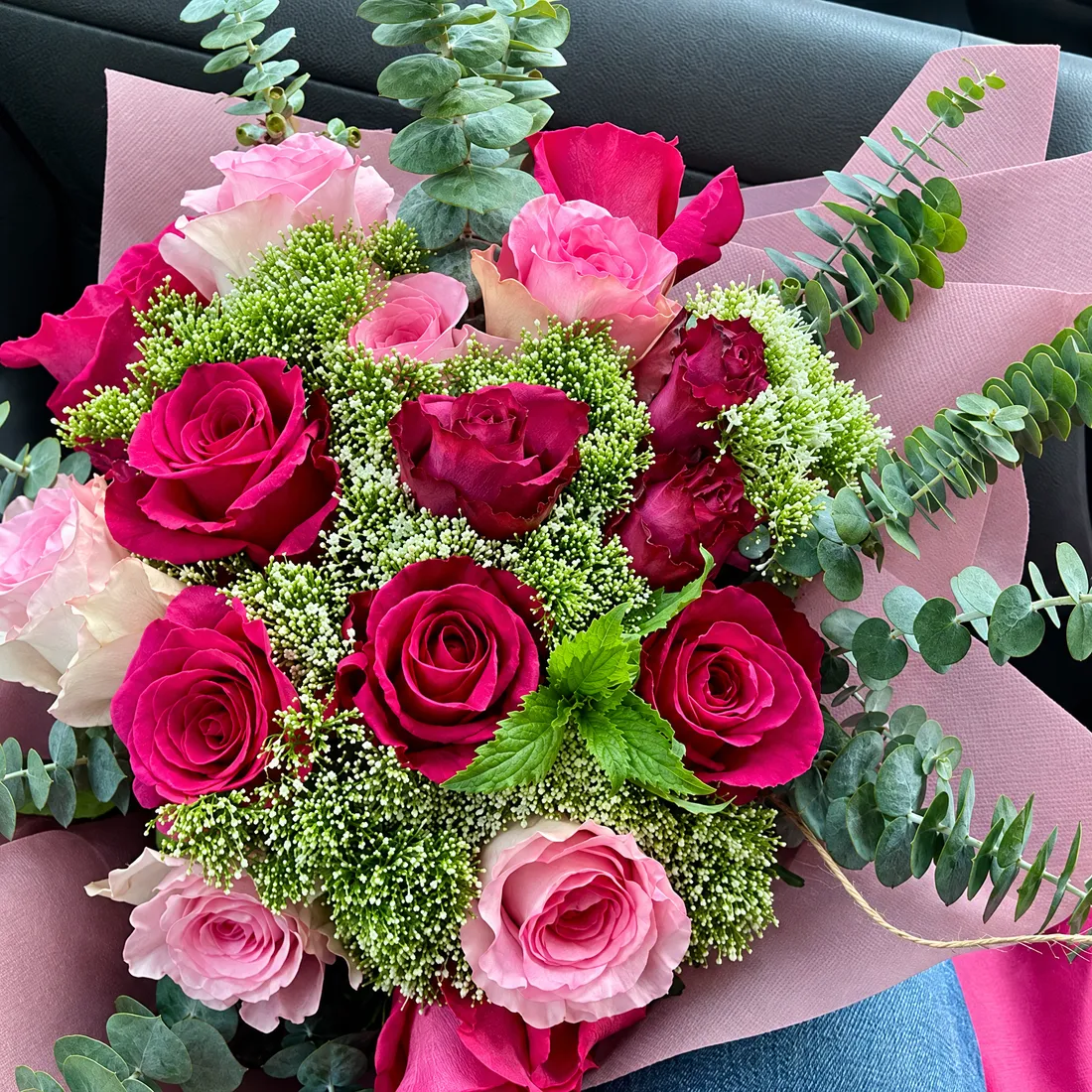 A wrapped bouquet of red and pink roses with eucalyptus