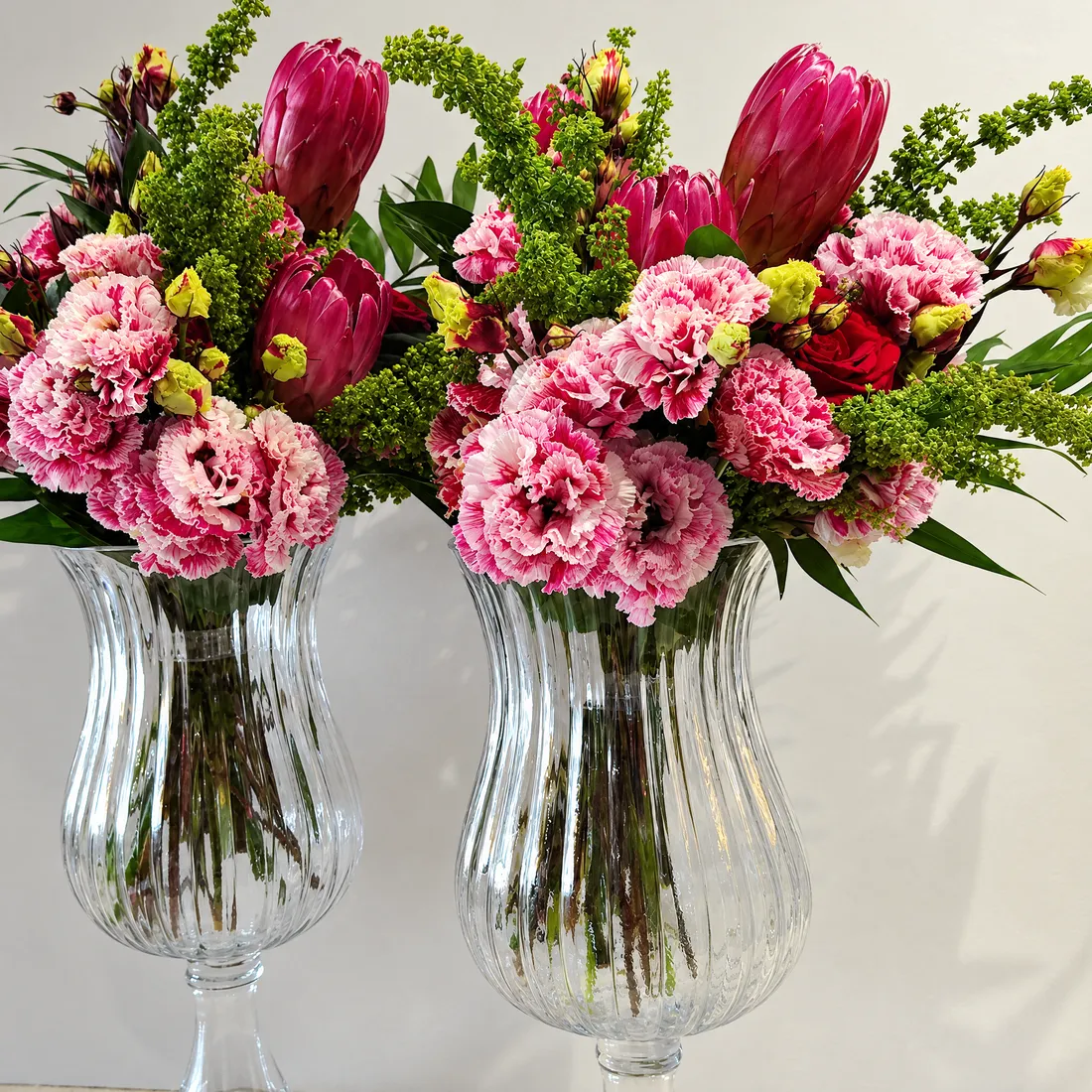 Two glass vases with pink protea, lisianthus, red roses and solidago