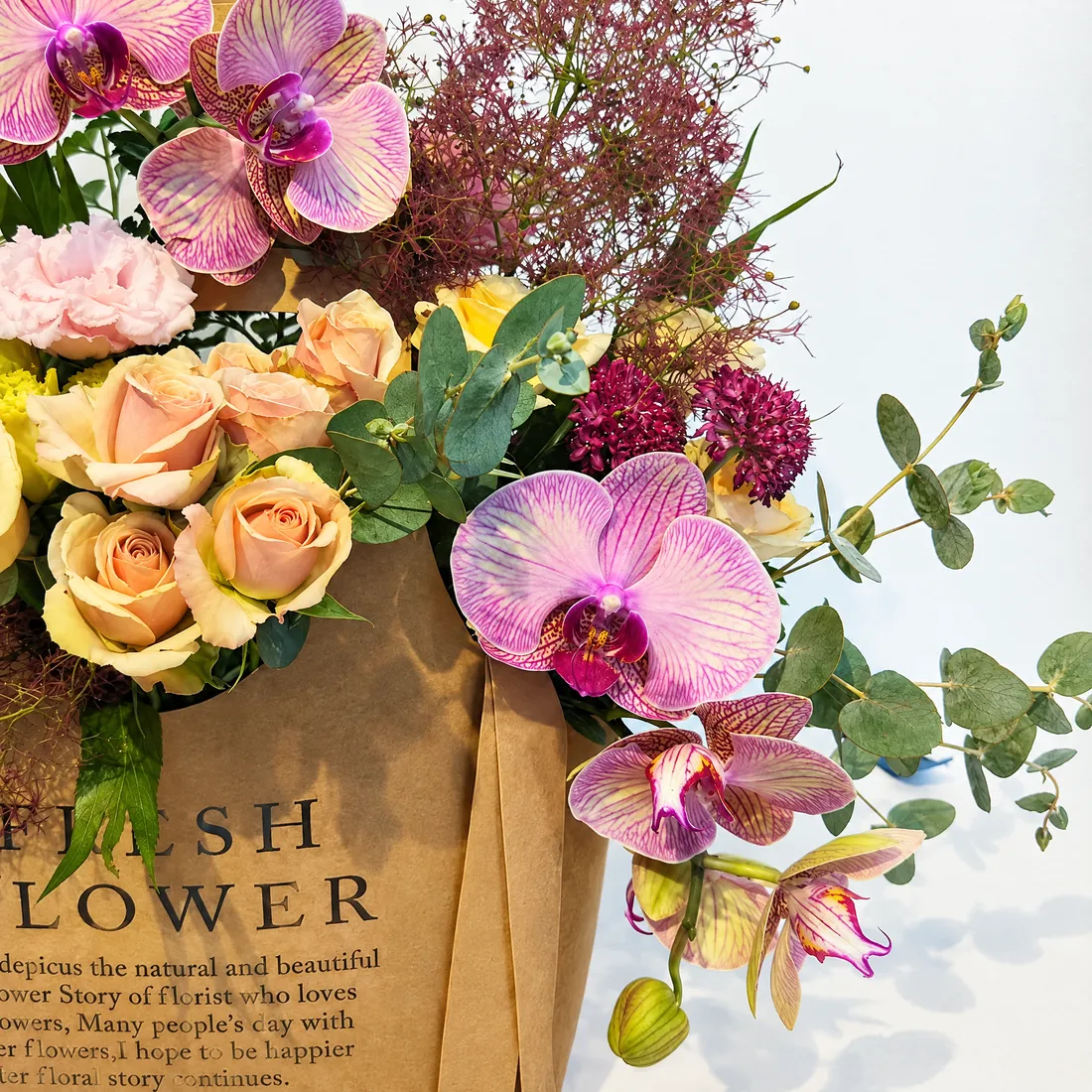 Pink orchids, peach roses and eucalyptus in a kraft gift bag